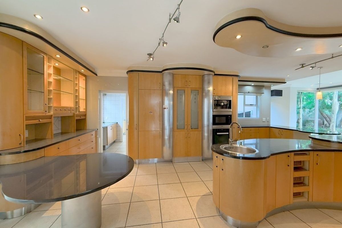 Spacious kitchen featuring custom curved cabinetry, stone countertops, integrated appliances, and a central island with a secondary sink.
