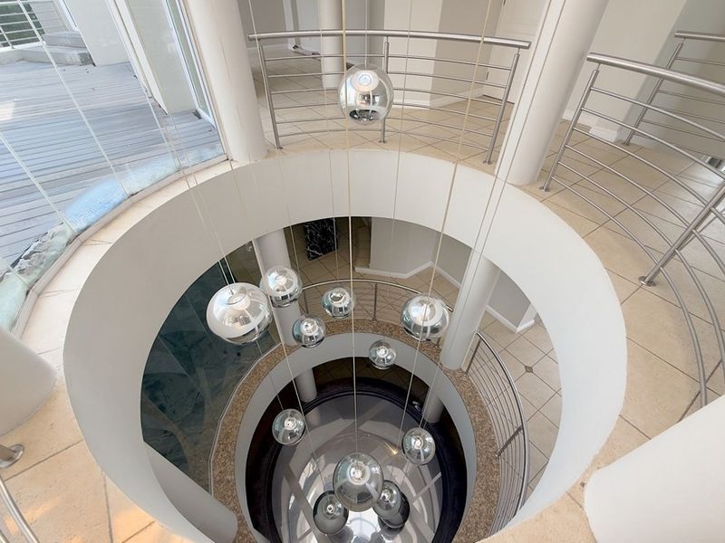 A grand circular entrance hall featuring a striking staircase with stainless steel balustrades and a modern multi-pendant light fixture.