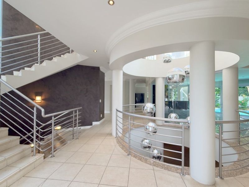 Spacious landing area featuring a striking curved staircase with stainless steel balustrades, tiled flooring, and architectural columns overlooking the lower level.