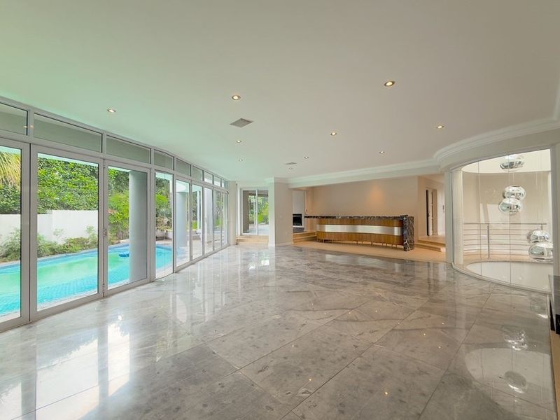 Spacious, light-filled living area featuring polished marble floors, a built-in bar, and expansive glass doors opening directly onto the pool area.