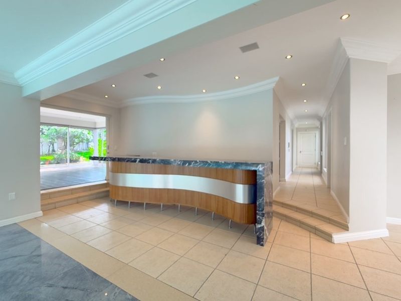 A spacious interior area featuring a modern built-in bar with a marble countertop, recessed lighting, and tiled flooring with stepped transitions.