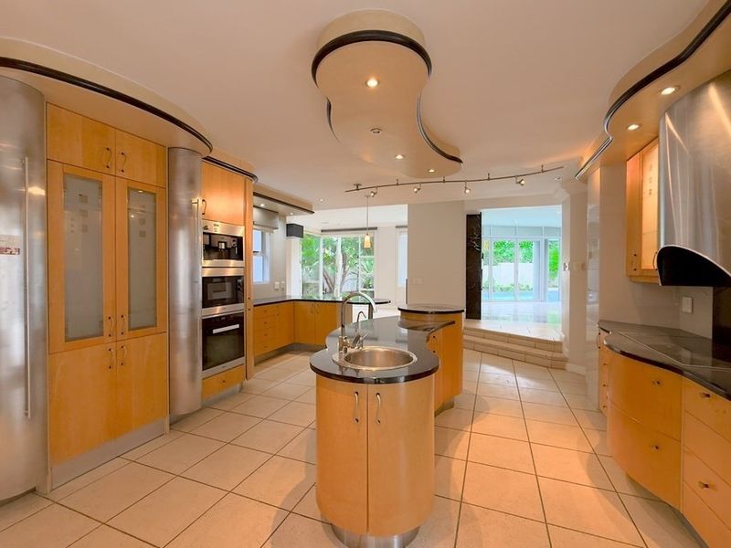 Spacious kitchen featuring custom curved light wood cabinetry, granite countertops, a central island with sink, and integrated stainless steel appliances.