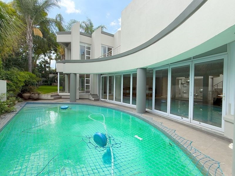 A modern rear exterior view featuring a curved swimming pool, expansive sliding glass doors, and a covered patio area.
