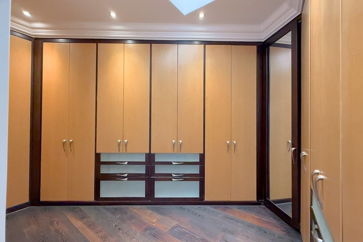 A spacious bedroom featuring extensive built-in cabinetry with integrated drawers, recessed lighting, a skylight, and rich hardwood flooring.