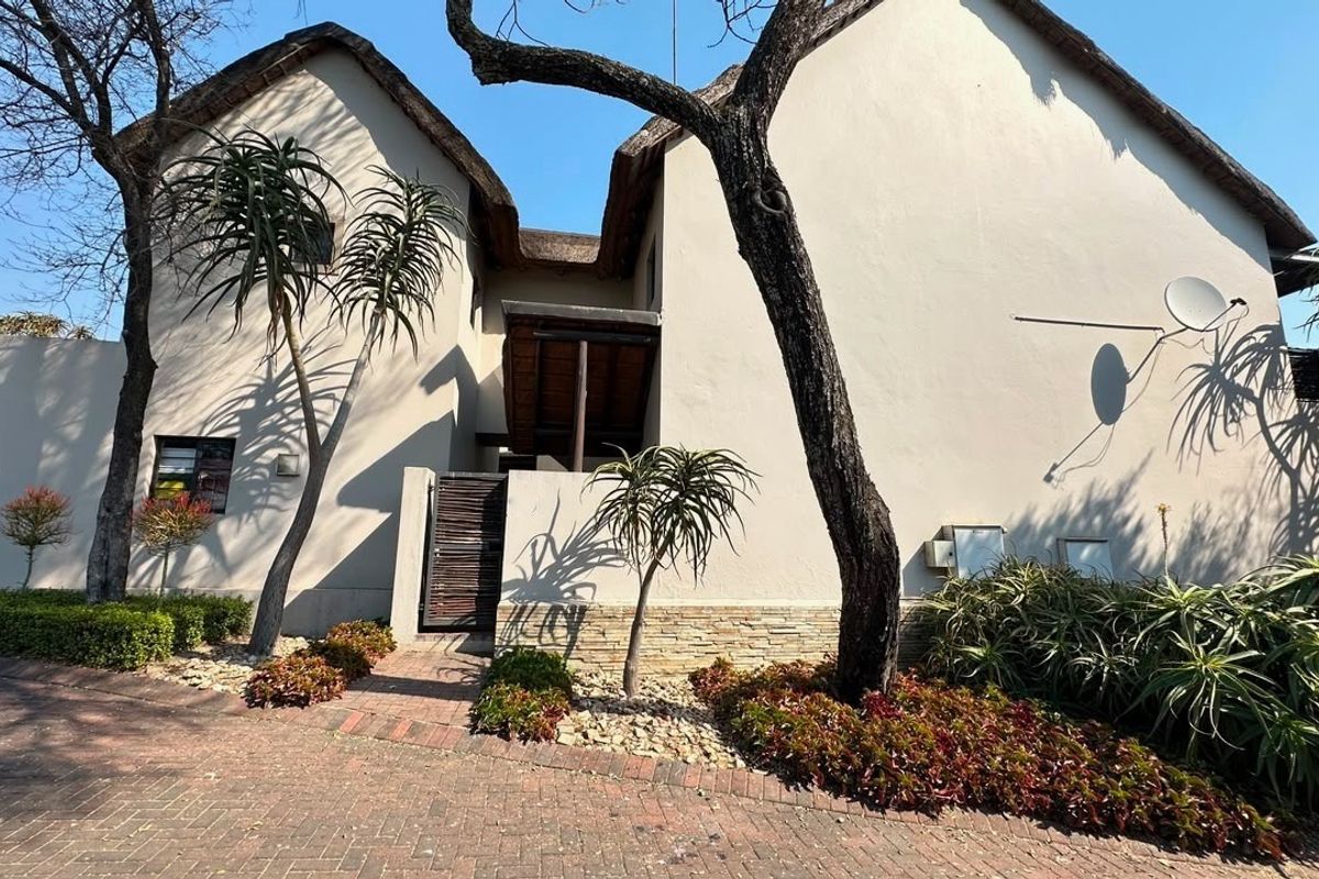 Front elevation of a house featuring a distinctive thatched roof, stone cladding accents, and a paved driveway with established garden landscaping.