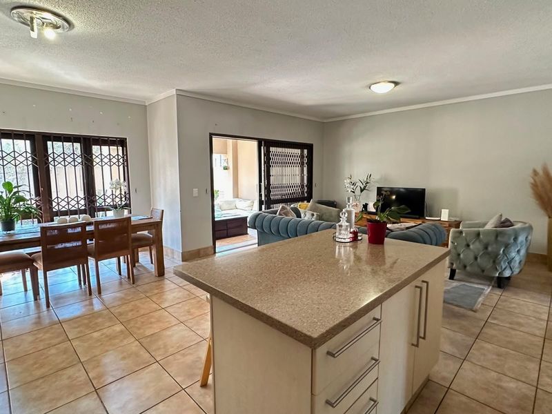 Spacious open-plan living and dining area featuring a central kitchen island with stone countertops and ceramic tiled flooring throughout.