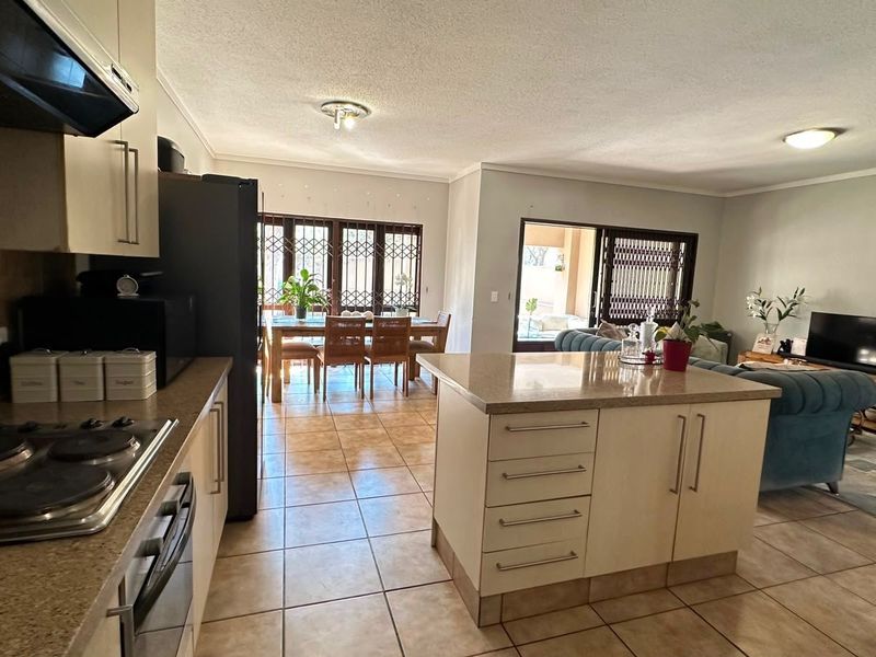 Open-plan living area featuring a kitchen with a central island, built-in appliances, and tiled flooring, flowing into a dining and lounge space.