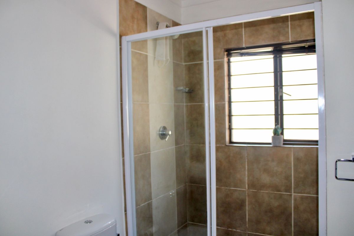 A functional bathroom featuring a shower enclosure with tiled walls, a toilet, and a window with security bars.