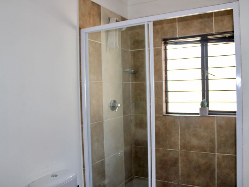 A functional bathroom featuring a shower enclosure with tiled walls, a toilet, and a window with security bars.
