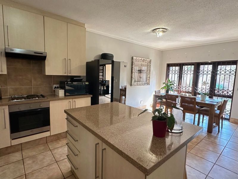 Open-plan kitchen and dining area featuring a central island, built-in oven, gas hob, and tiled flooring with access to the exterior via security gates.
