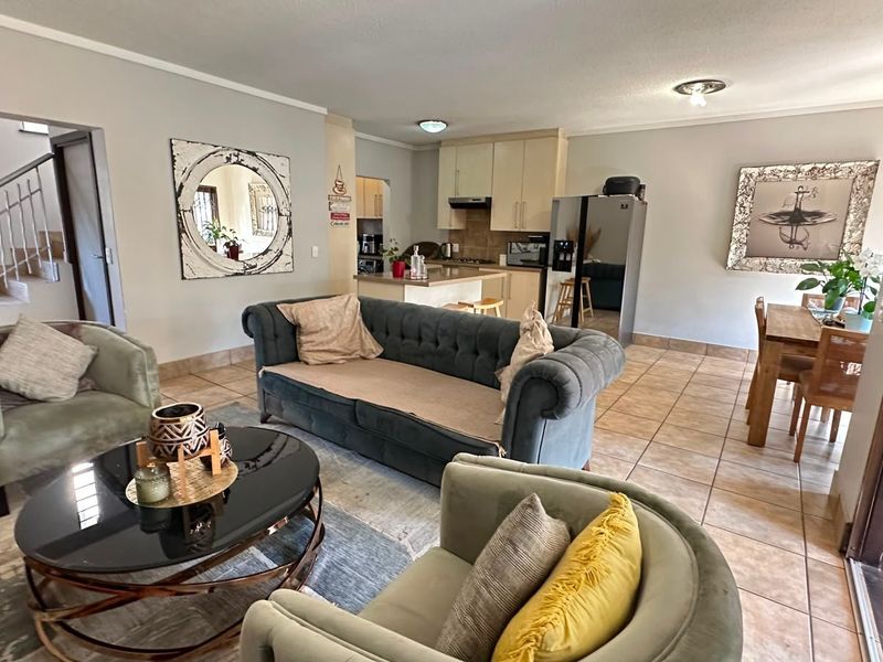 Open-plan living and dining area featuring tiled flooring, integrated kitchen cabinetry, and a staircase leading to the upper level.