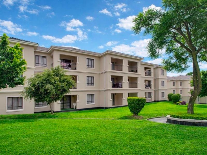 A view of the rear apartment building facade featuring multiple balconies, well-maintained green lawns, and landscaped garden areas.