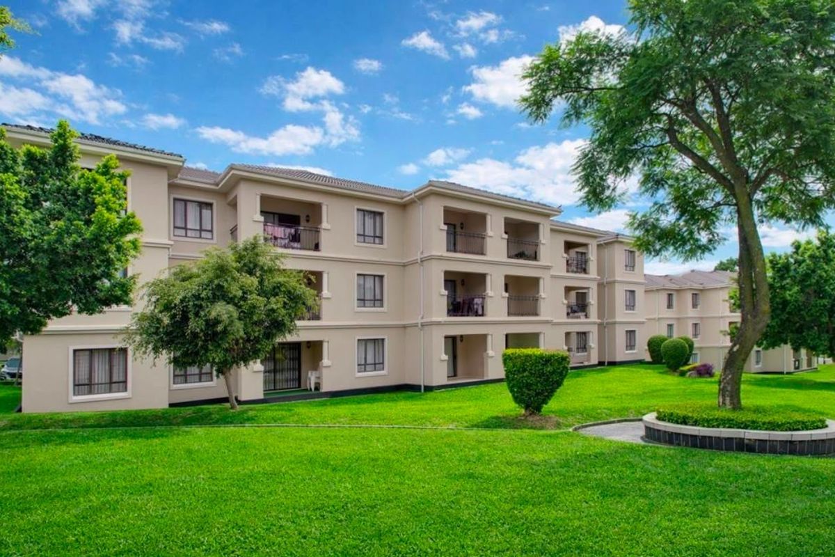 A view of the rear apartment building facade featuring multiple balconies, well-maintained green lawns, and landscaped garden areas.