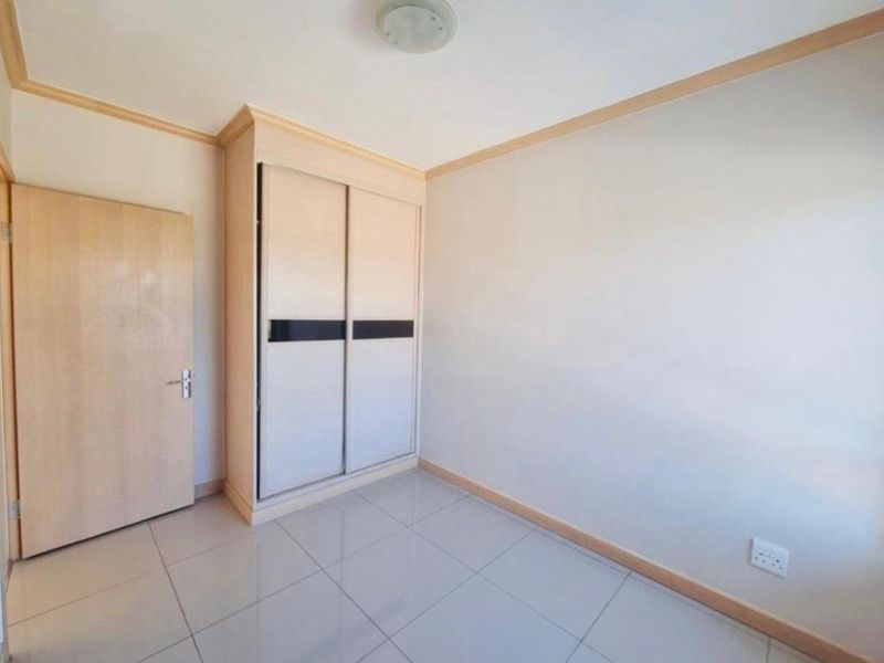 A clean, empty bedroom featuring neutral tiled flooring, light wood-toned trim, and a built-in sliding door wardrobe.