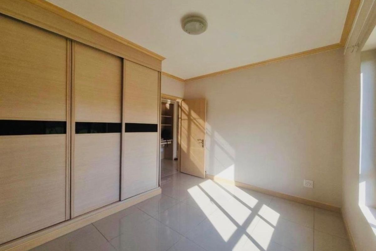 A bright, empty bedroom featuring neutral tiled flooring, built-in sliding door wardrobes, and classic cove cornicing, offering a clean and versatile living space.
