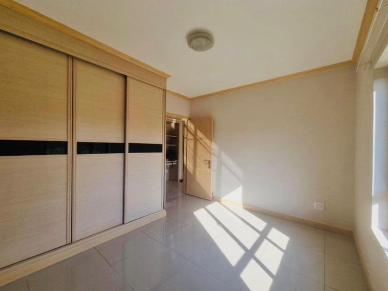 A bright, empty bedroom featuring neutral tiled flooring, built-in sliding door wardrobes, and classic cove cornicing, offering a clean and versatile living space.