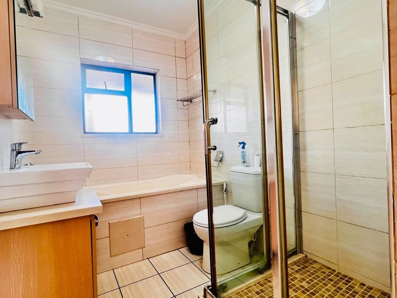 A functional bathroom featuring a built-in bathtub, separate shower enclosure, vessel sink vanity, and neutral wall tiling.