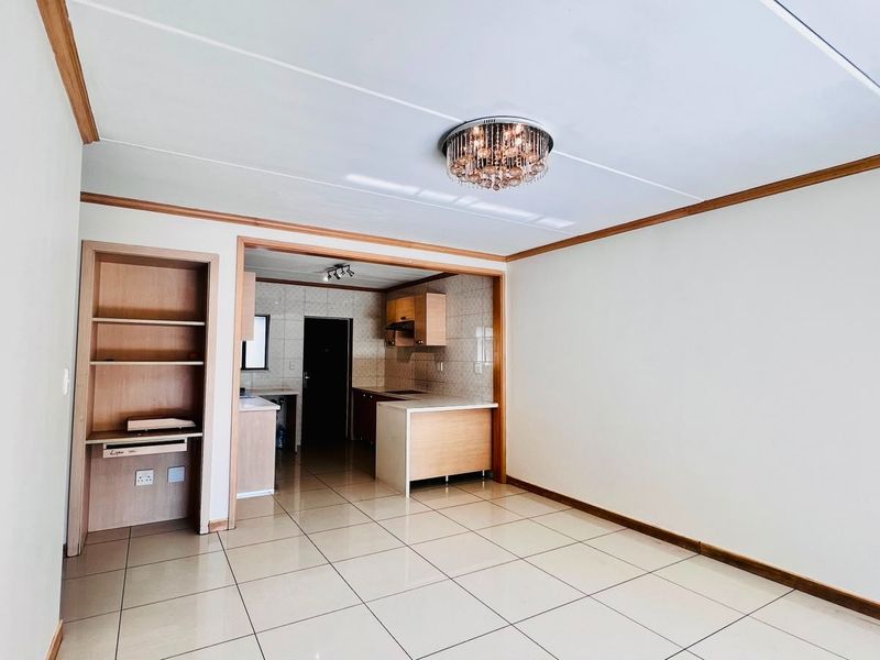 An open-plan living and kitchen area featuring tiled flooring, built-in cabinetry, and a dedicated shelving unit, offering a clean and functional layout.