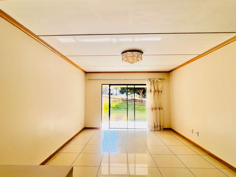An empty, well-lit living room featuring tiled flooring, crown molding, and a sliding glass door providing access to the outdoor area.