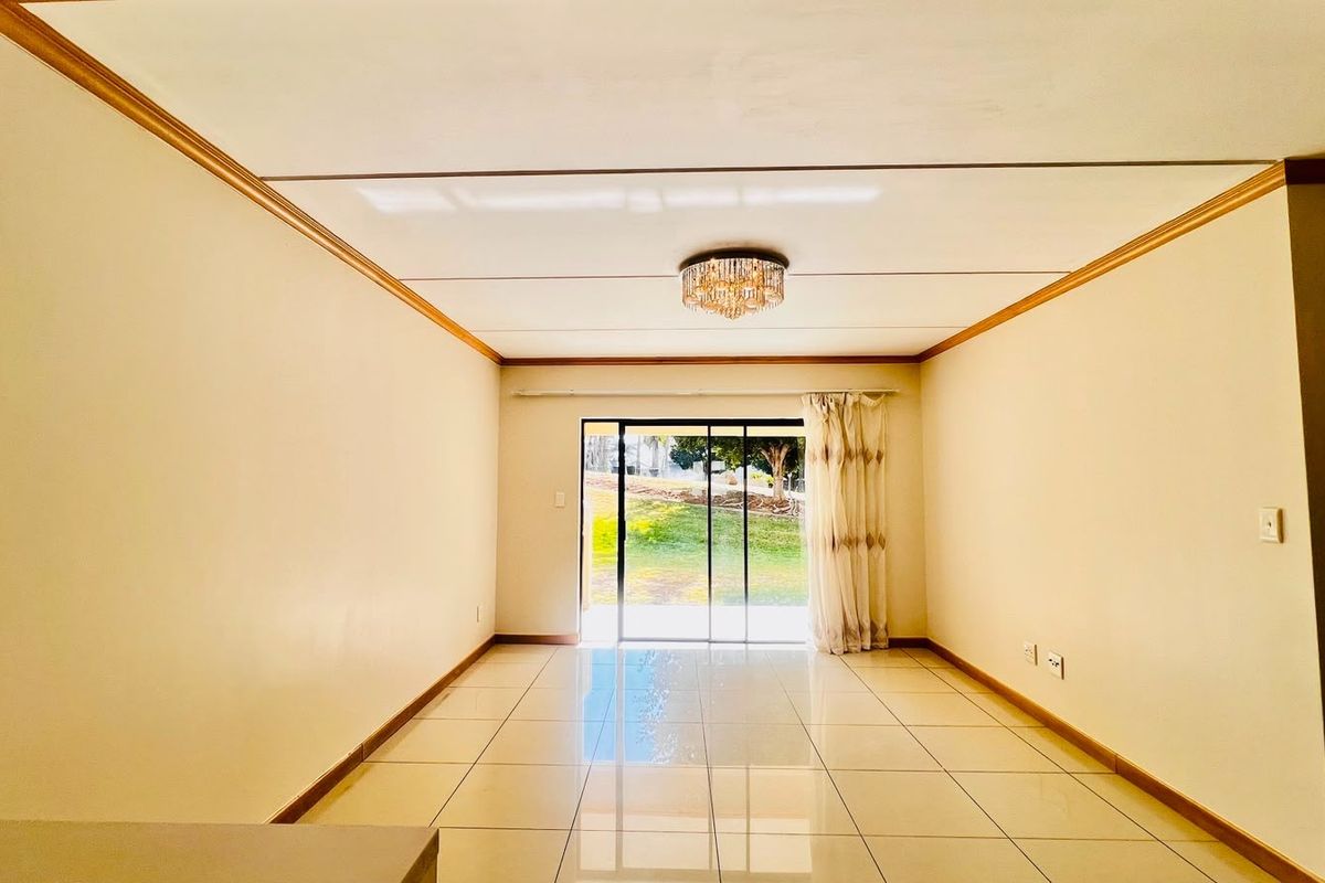 An empty, well-lit living room featuring tiled flooring, crown molding, and a sliding glass door providing access to the outdoor area.