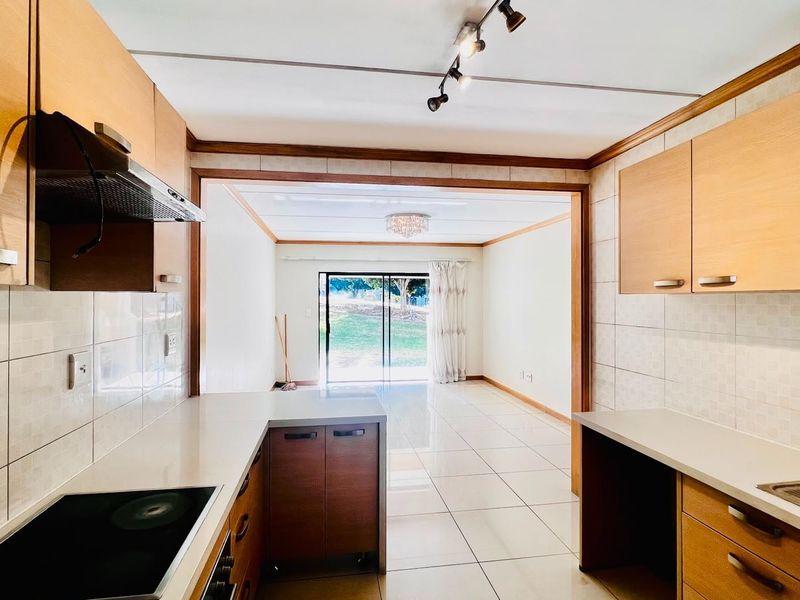Open-plan kitchen and living area featuring light wood cabinetry, tiled flooring, and direct access to an outdoor space through sliding glass doors.