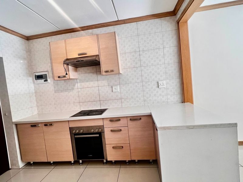 A clean, functional kitchen featuring light wood cabinetry, stone countertops, a built-in oven, electric hob, and a tiled backsplash.