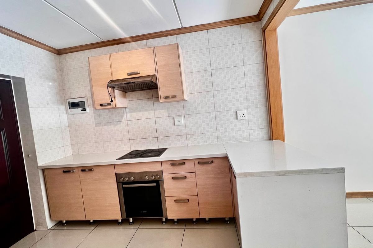 A clean, functional kitchen featuring light wood cabinetry, stone countertops, a built-in oven, electric hob, and a tiled backsplash.
