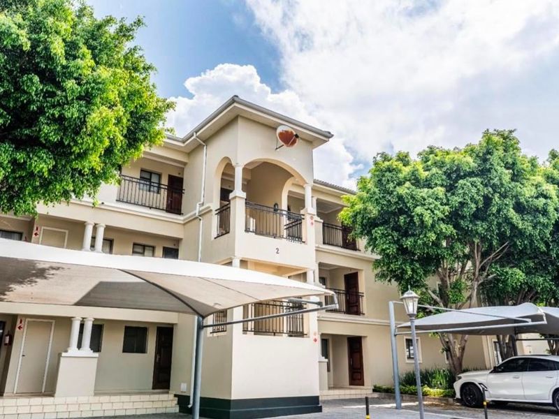 Front elevation of a multi-story apartment complex featuring balconies with wrought iron railings and covered parking bays.
