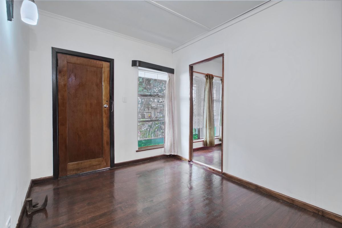 An empty living area featuring dark timber flooring, a solid timber door, and a louver window, providing a blank canvas for renovation.