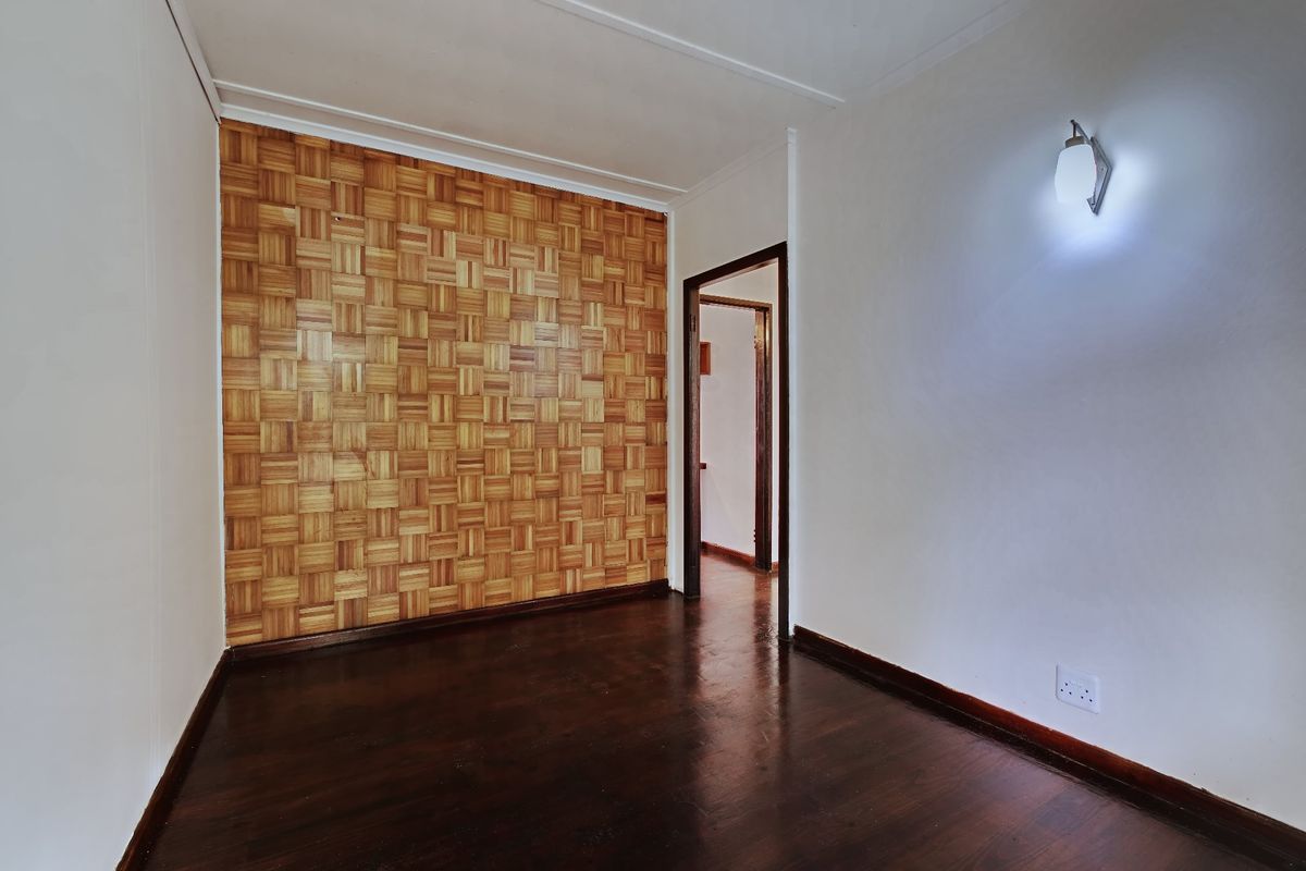 An empty bedroom featuring dark parquet wood flooring, a decorative timber-paneled feature wall, and a wall-mounted light fixture.