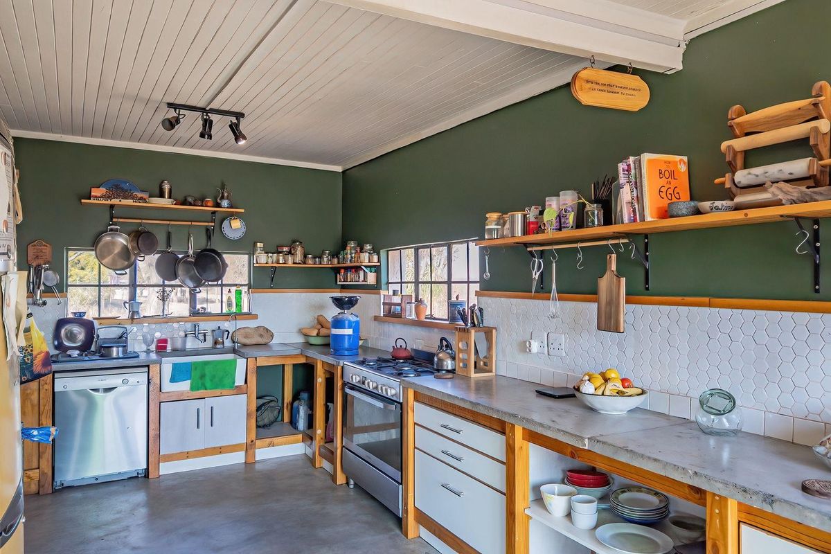A rustic farmhouse kitchen featuring concrete countertops, a farmhouse sink, open timber shelving, and a gas stove with a tiled backsplash.