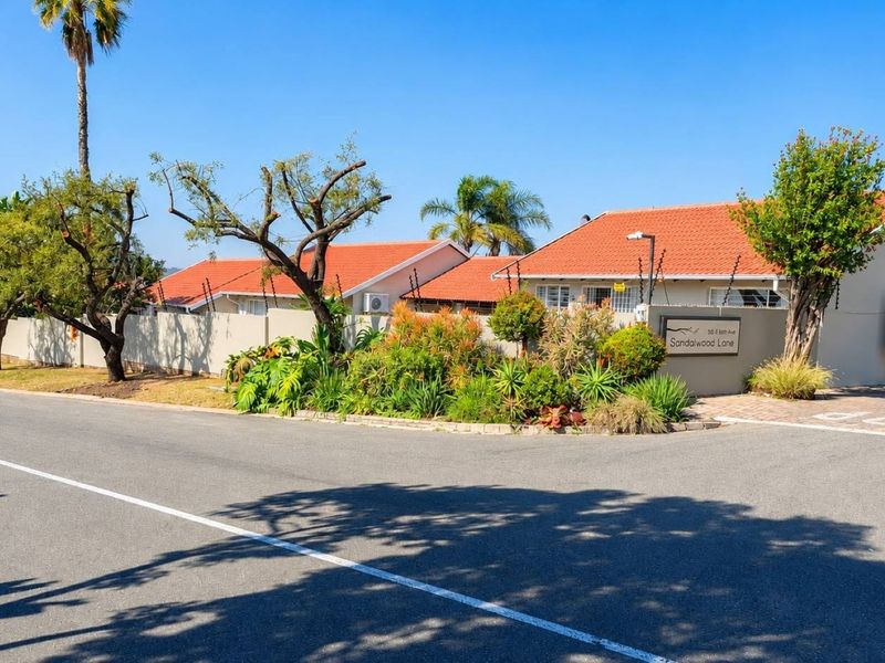 Street view of the property entrance featuring a perimeter wall with electric fencing and established landscaping.
