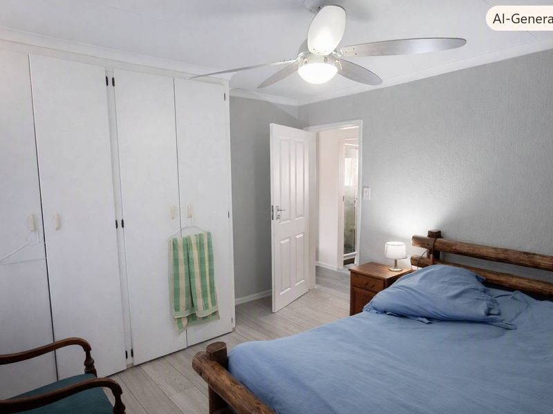 A well-maintained bedroom featuring built-in cupboards, a ceiling fan, and light-toned laminate flooring, with an adjoining doorway leading to an ensuite.