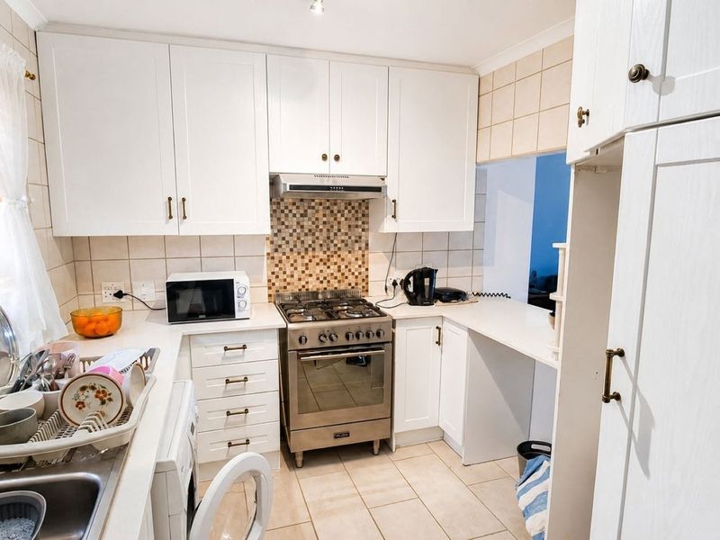 A functional kitchen featuring white cabinetry, a gas stove with extractor fan, tiled backsplash, and tiled flooring with a convenient pass-through window.