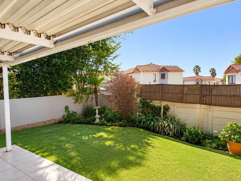 A well-maintained covered patio overlooking a private, landscaped garden with a neat lawn and secure boundary fencing.