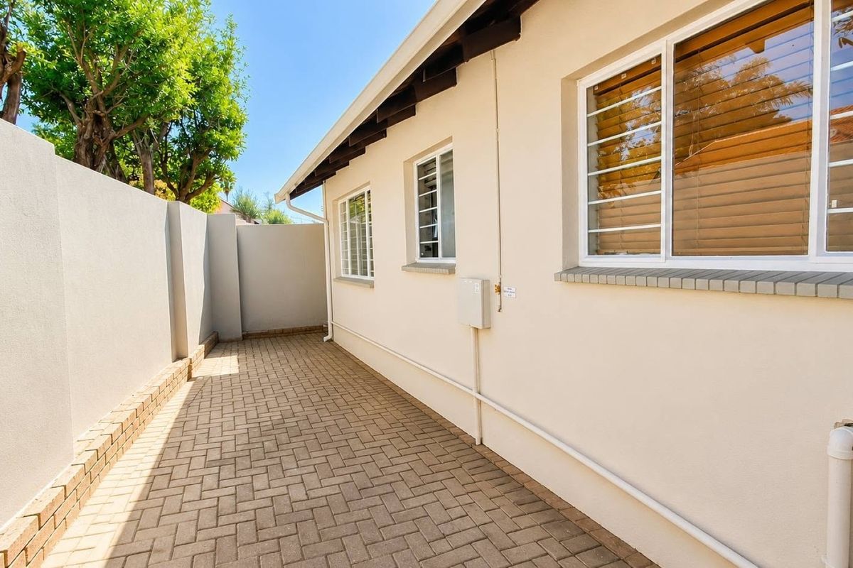 A clean, paved side walkway featuring a secure boundary wall, external electrical infrastructure, and windows fitted with security bars.