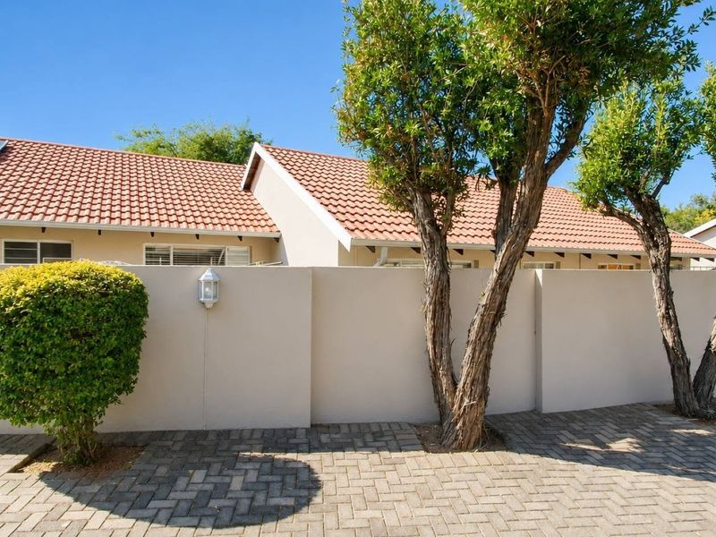Front exterior view of the property featuring a paved driveway, boundary wall, and terracotta tiled roof with integrated solar panels.