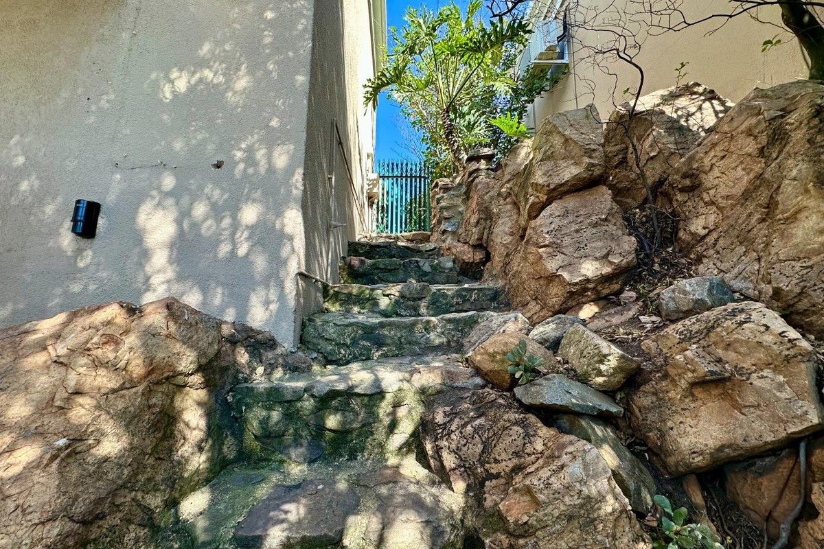 Exterior stone staircase leading to a rear garden gate, flanked by natural rock formations and the side of the property.
