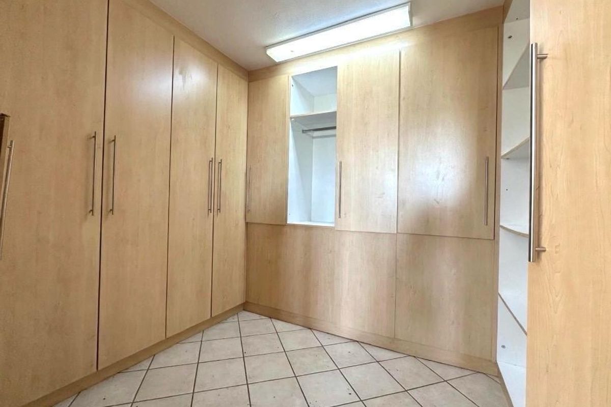 A walk-in closet or bedroom area featuring extensive built-in light wood cabinetry and tiled flooring.