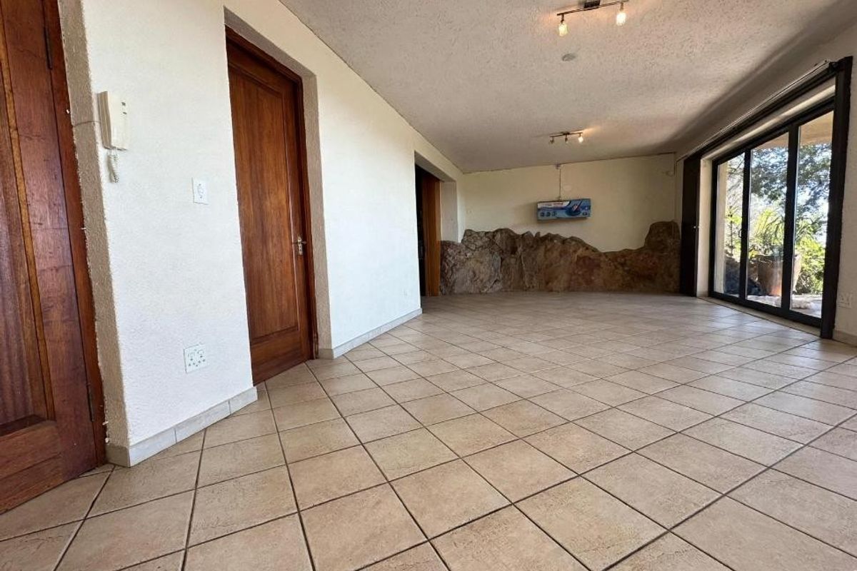 Spacious living area featuring tiled flooring, sliding glass doors leading outdoors, and a unique natural rock feature wall.