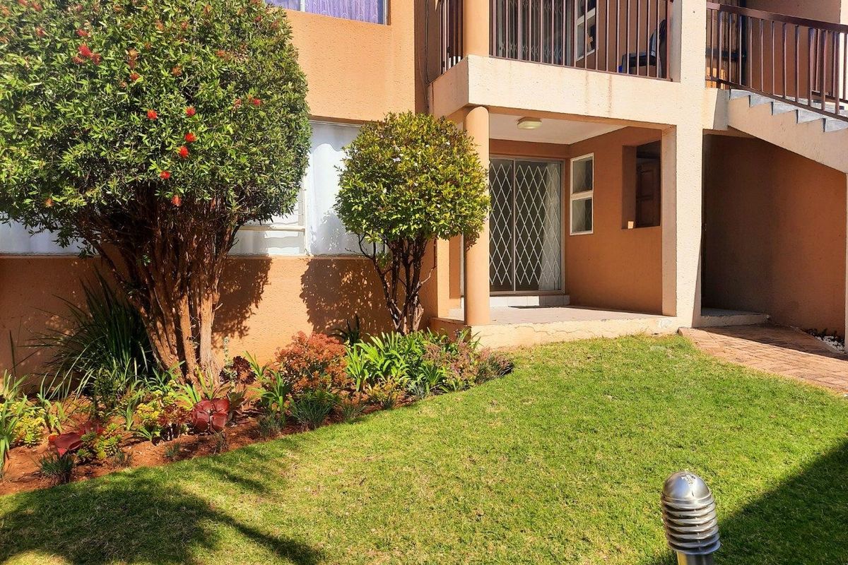 Ground floor apartment exterior featuring a small private garden, paved walkway, and a covered patio area with security gate access.