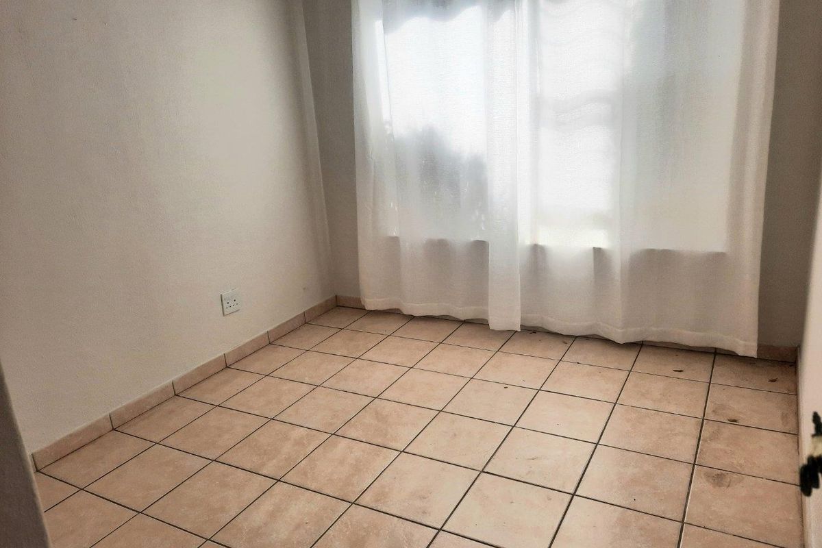 An empty bedroom featuring neutral tiled flooring and a window with sheer curtains, offering a blank canvas for potential interior design updates.