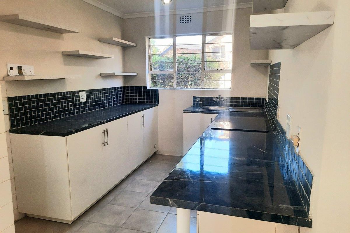 A functional, empty kitchen featuring dark stone-look countertops, white cabinetry, tiled backsplash, and floating shelving, offering a clean canvas for updates.