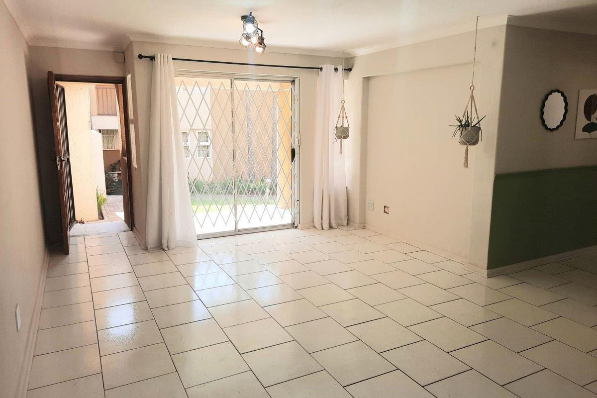 A bright, open-plan living area featuring neutral tiled flooring, a sliding glass door with security gate, and direct access to an outdoor space.
