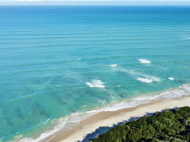 An aerial view of the pristine coastline featuring turquoise ocean waters, a sandy beach, and natural coastal vegetation.