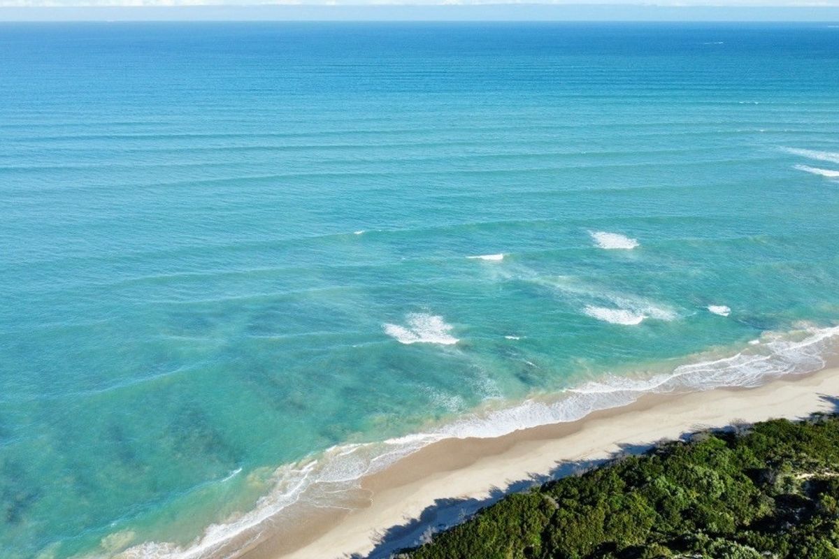 An aerial view of the pristine coastline featuring turquoise ocean waters, a sandy beach, and natural coastal vegetation.