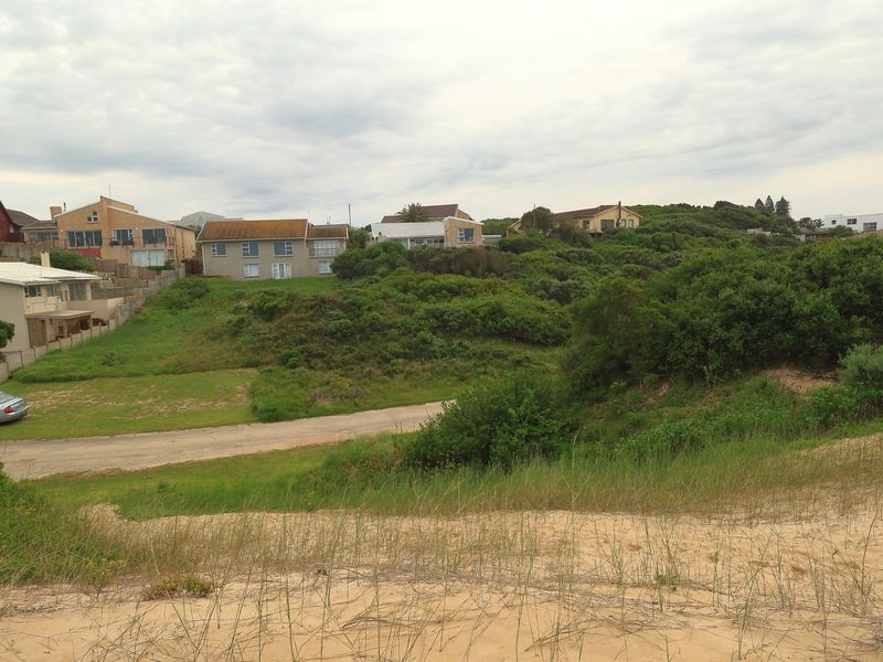 A view of the vacant residential land featuring natural sand dunes, coastal vegetation, and an unpaved access road with surrounding residential properties.