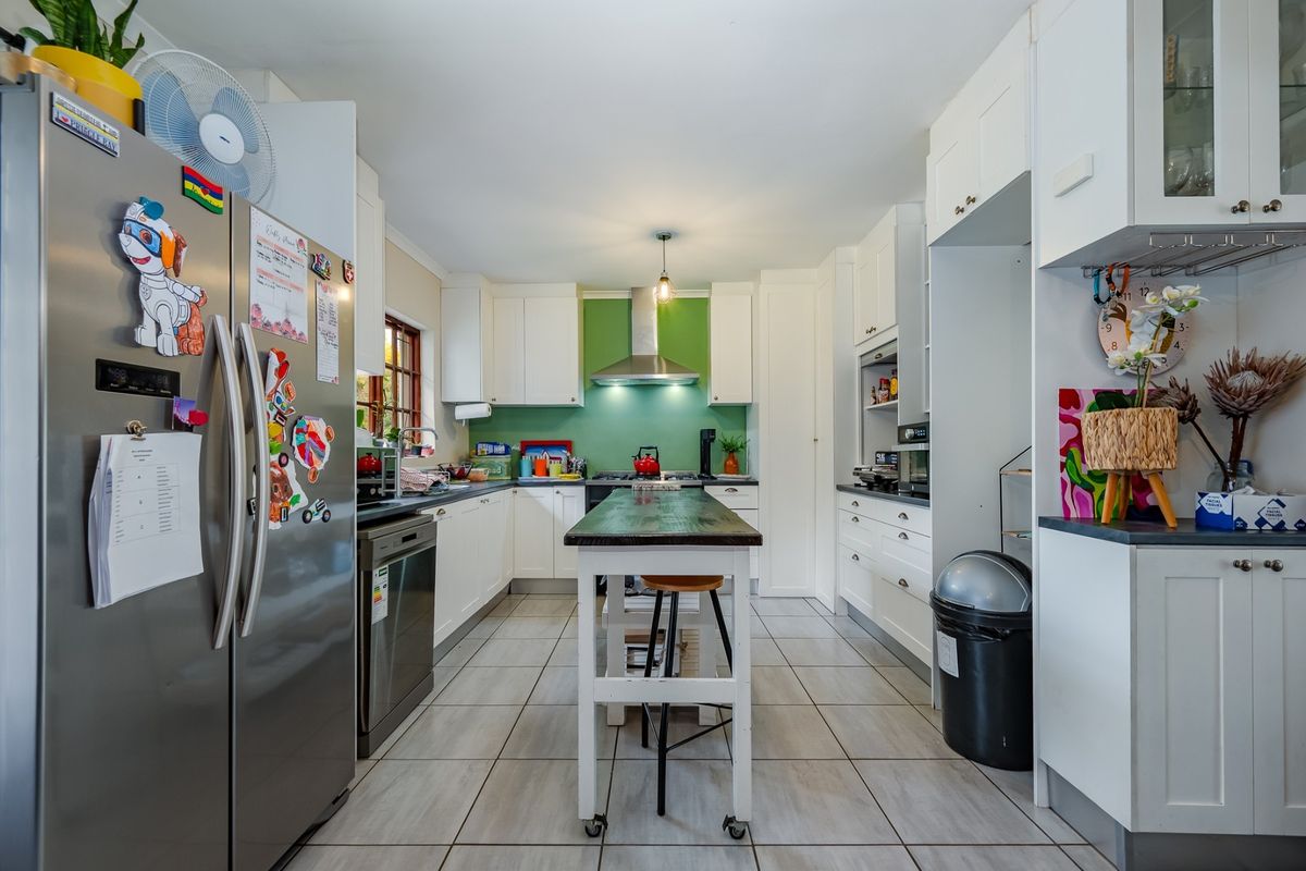 A functional kitchen featuring white cabinetry, a vibrant green splashback, stainless steel extractor fan, and tiled flooring with a central prep island.