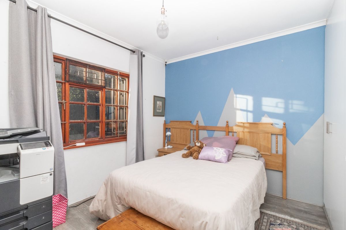 A bedroom featuring laminate flooring, a timber-framed window, and a built-in wardrobe, offering a functional space with potential for cosmetic updates.
