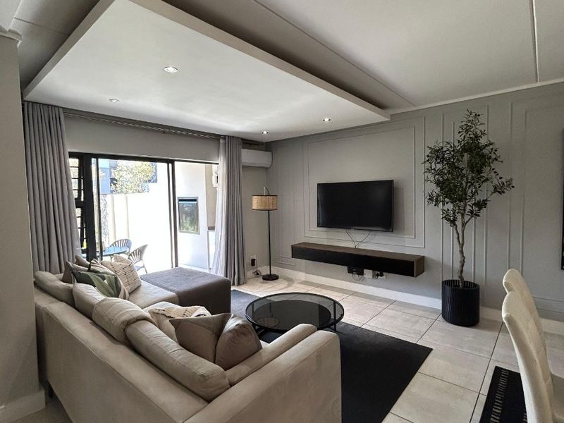 Modern living room featuring elegant wall paneling, a floating media console, recessed ceiling lighting, and large sliding doors leading to an outdoor patio area.